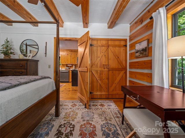 bedroom with light wood-type flooring, ceiling fan, ensuite bathroom, and wooden walls