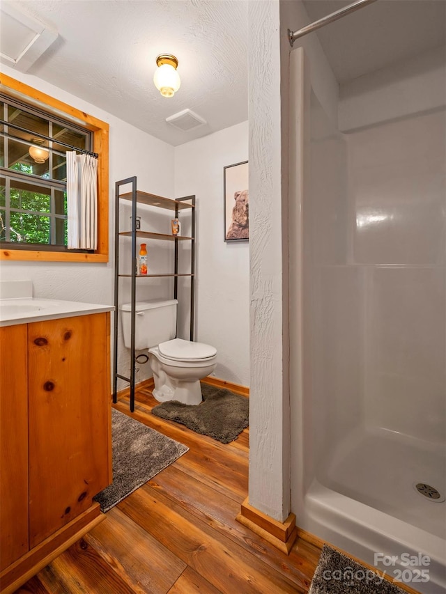 bathroom featuring hardwood / wood-style floors, toilet, walk in shower, and vanity