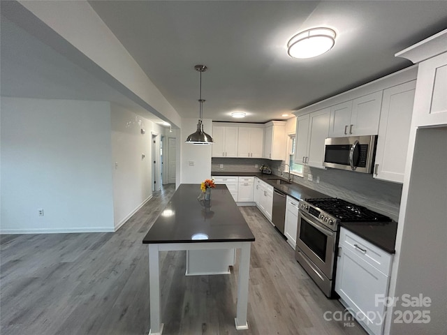 kitchen with pendant lighting, sink, appliances with stainless steel finishes, white cabinetry, and light hardwood / wood-style floors