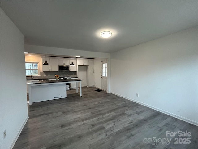 kitchen with appliances with stainless steel finishes, pendant lighting, white cabinetry, backsplash, and dark hardwood / wood-style flooring