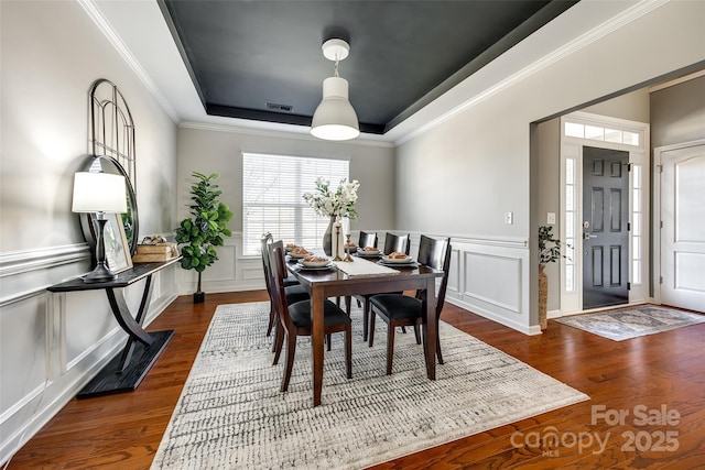 dining space featuring a raised ceiling, ornamental molding, and dark hardwood / wood-style floors