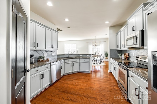 kitchen featuring appliances with stainless steel finishes, white cabinetry, dark hardwood / wood-style floors, decorative light fixtures, and kitchen peninsula