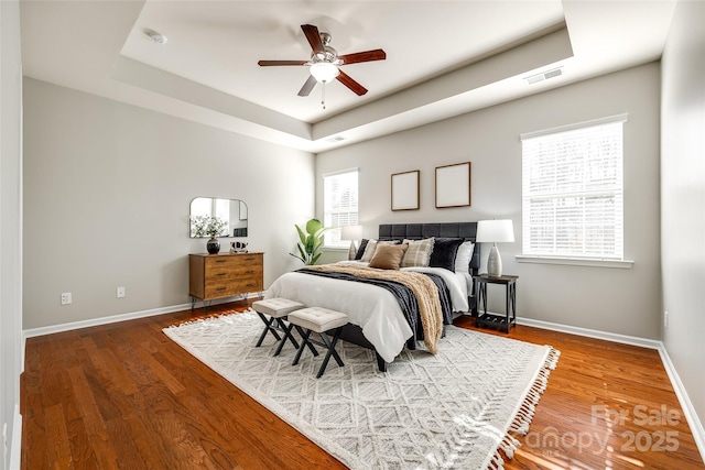 bedroom with wood-type flooring, ceiling fan, and a tray ceiling