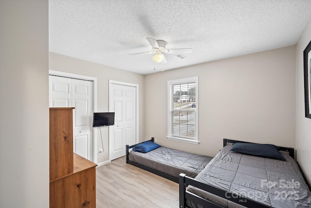 bedroom with ceiling fan, light wood-type flooring, a textured ceiling, and two closets