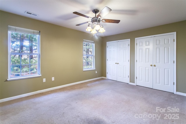 unfurnished bedroom with multiple windows, two closets, and light carpet