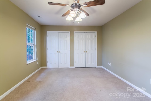 unfurnished bedroom featuring light carpet, ceiling fan, and multiple closets