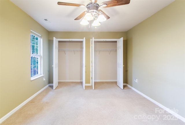 unfurnished bedroom with two closets, light colored carpet, and ceiling fan