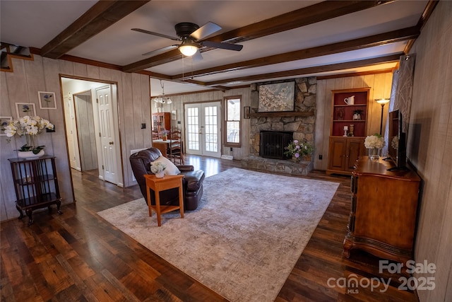 living room with dark wood-type flooring, french doors, a stone fireplace, wood walls, and beam ceiling