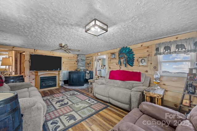 living room with ceiling fan, wood walls, hardwood / wood-style floors, and a wood stove