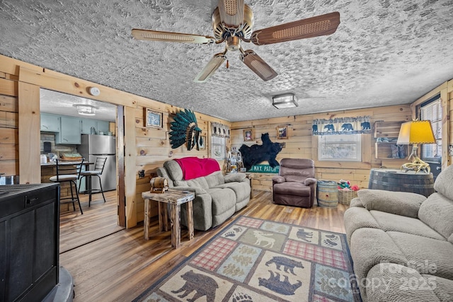 living room with hardwood / wood-style flooring, ceiling fan, and wooden walls