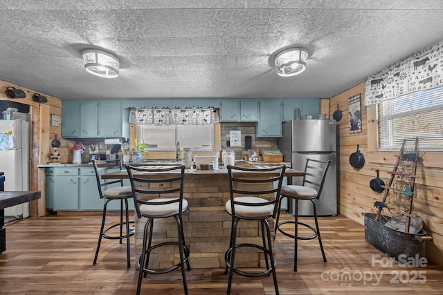 kitchen featuring white refrigerator, dark hardwood / wood-style flooring, wooden walls, stainless steel fridge, and blue cabinets