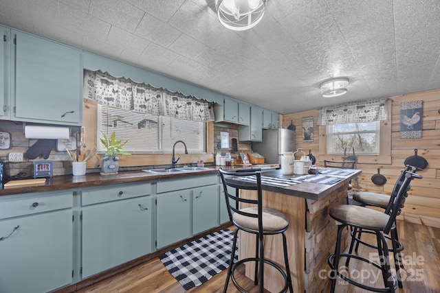 kitchen with wooden counters, sink, dark hardwood / wood-style floors, wood walls, and stainless steel refrigerator