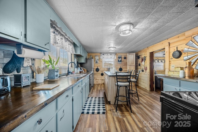 kitchen with butcher block counters, a kitchen bar, hardwood / wood-style flooring, wooden walls, and sink