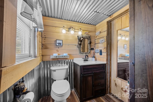 bathroom featuring hardwood / wood-style floors, toilet, vanity, and wooden walls