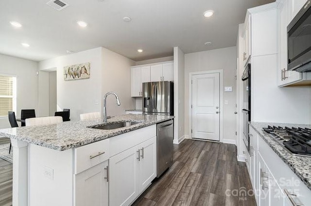 kitchen with sink, stainless steel appliances, light stone counters, white cabinets, and a center island with sink