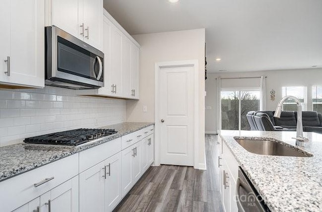 kitchen featuring appliances with stainless steel finishes, sink, white cabinets, dark hardwood / wood-style flooring, and light stone countertops