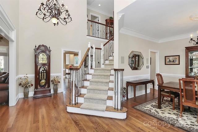 entryway with an inviting chandelier, crown molding, wood-type flooring, and a towering ceiling