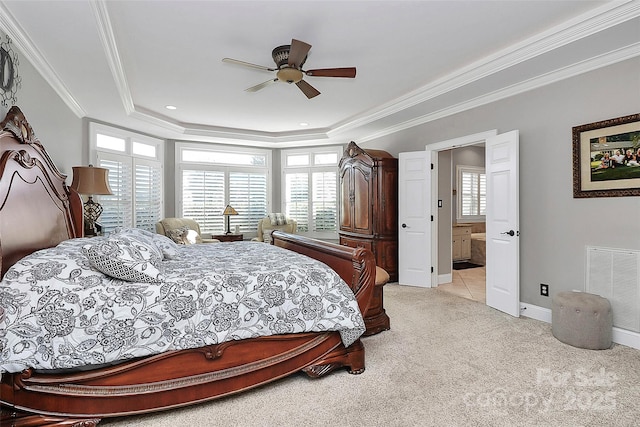 carpeted bedroom featuring crown molding, ceiling fan, ensuite bath, and a tray ceiling