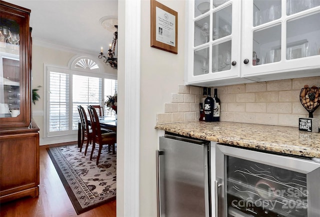 bar with wine cooler, ornamental molding, stainless steel fridge, light stone countertops, and backsplash