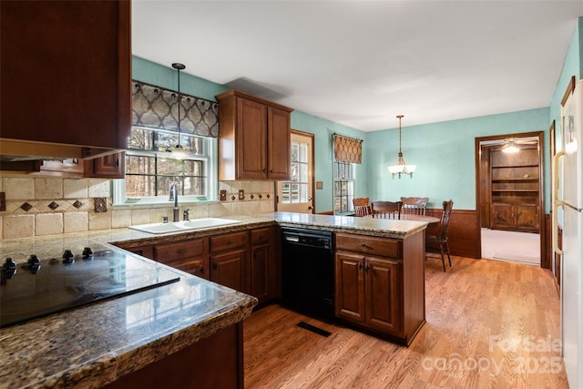 kitchen with kitchen peninsula, decorative light fixtures, sink, light hardwood / wood-style floors, and black appliances