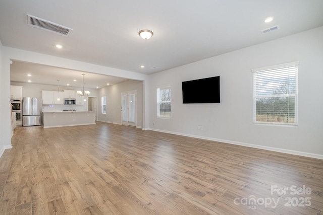 unfurnished living room with an inviting chandelier and light hardwood / wood-style flooring