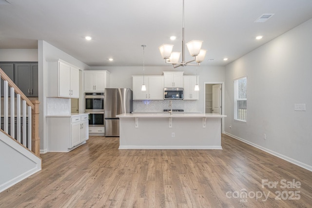 kitchen featuring white cabinetry, appliances with stainless steel finishes, decorative light fixtures, and a center island with sink