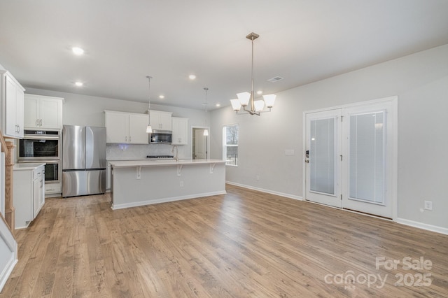 kitchen with pendant lighting, tasteful backsplash, white cabinetry, an island with sink, and stainless steel appliances