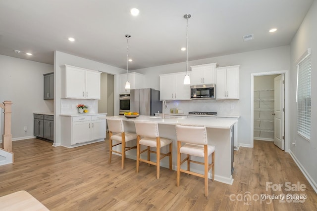 kitchen with white cabinets, decorative backsplash, a kitchen island with sink, light hardwood / wood-style floors, and stainless steel appliances