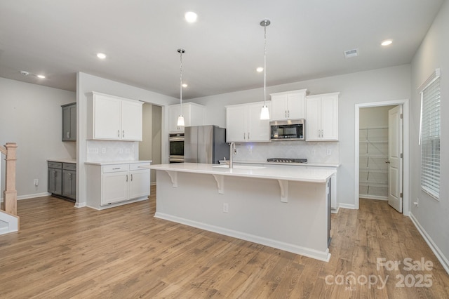 kitchen with a kitchen bar, white cabinetry, hanging light fixtures, an island with sink, and stainless steel appliances