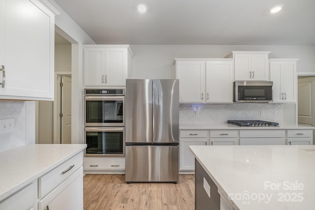 kitchen featuring stainless steel appliances, light stone countertops, light hardwood / wood-style flooring, and white cabinets