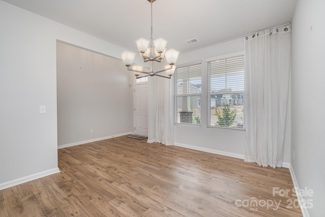 unfurnished dining area featuring an inviting chandelier and hardwood / wood-style floors