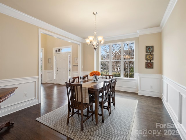 dining room with an inviting chandelier, dark wood-style floors, crown molding, and a wainscoted wall