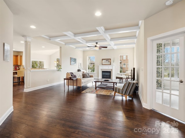 living room featuring coffered ceiling, baseboards, hardwood / wood-style floors, a glass covered fireplace, and decorative columns