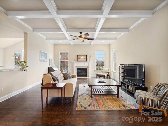 living area featuring beam ceiling, a glass covered fireplace, wood finished floors, baseboards, and ceiling fan with notable chandelier