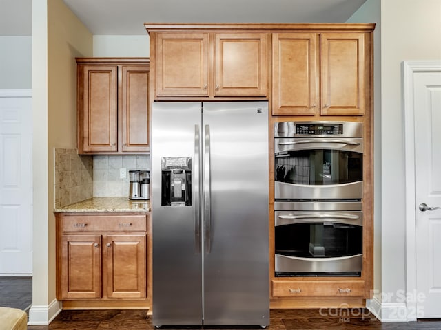 kitchen with light stone counters, dark wood-style floors, stainless steel appliances, decorative backsplash, and baseboards