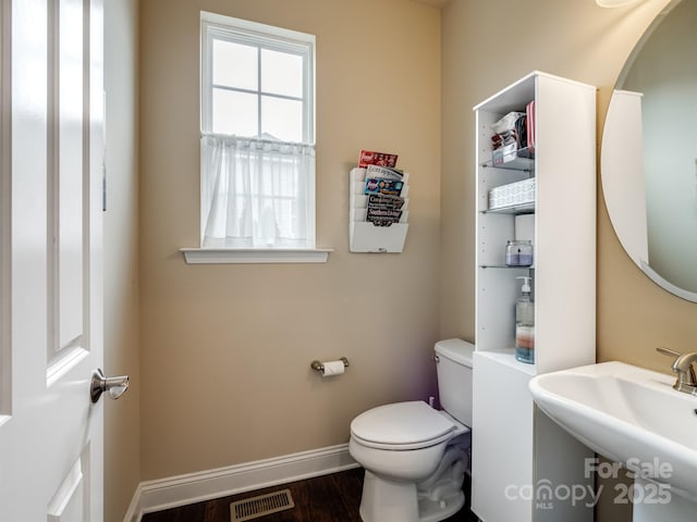 half bathroom featuring toilet, wood finished floors, a sink, visible vents, and baseboards