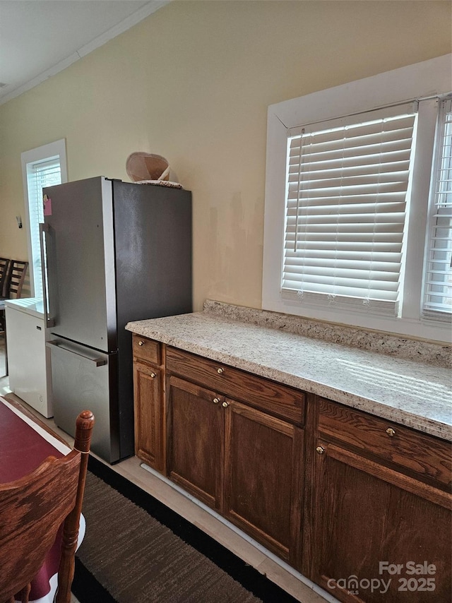 kitchen with stainless steel refrigerator, crown molding, dark brown cabinetry, and light stone countertops