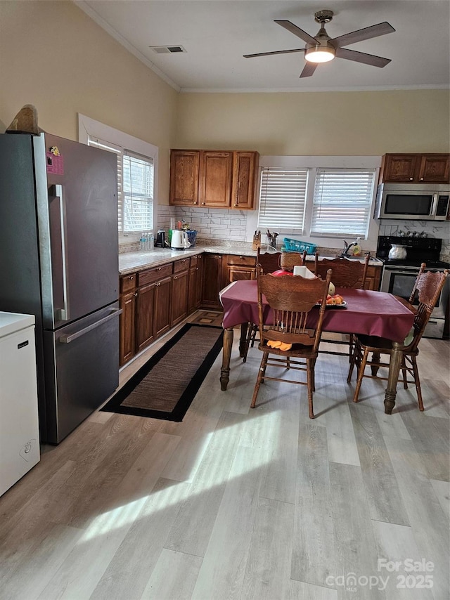 kitchen with tasteful backsplash, stainless steel appliances, crown molding, and light hardwood / wood-style floors