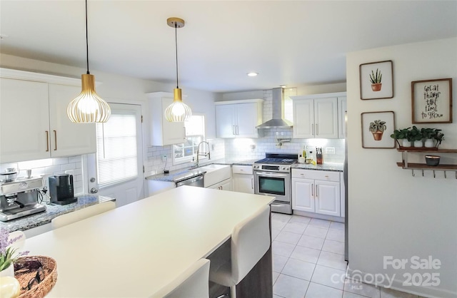 kitchen with tasteful backsplash, wall chimney range hood, white cabinets, decorative light fixtures, and stainless steel appliances