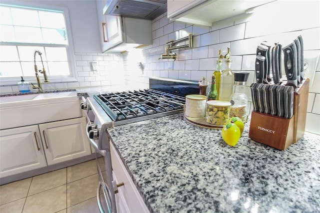 kitchen with light stone countertops, white cabinets, sink, stainless steel gas range oven, and light tile patterned floors