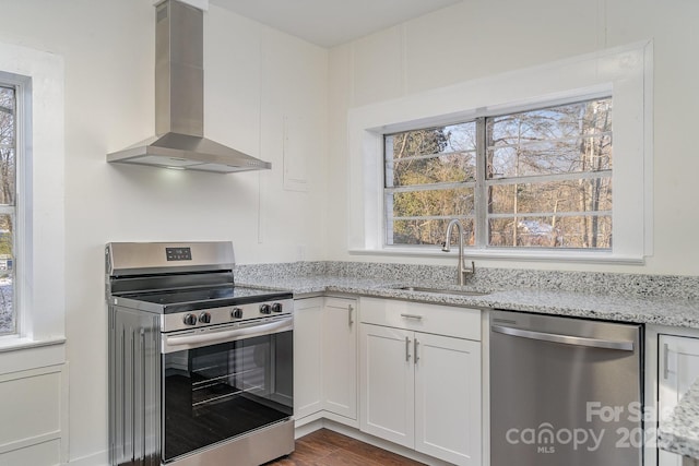 kitchen with wall chimney exhaust hood, sink, white cabinetry, stainless steel appliances, and light stone countertops