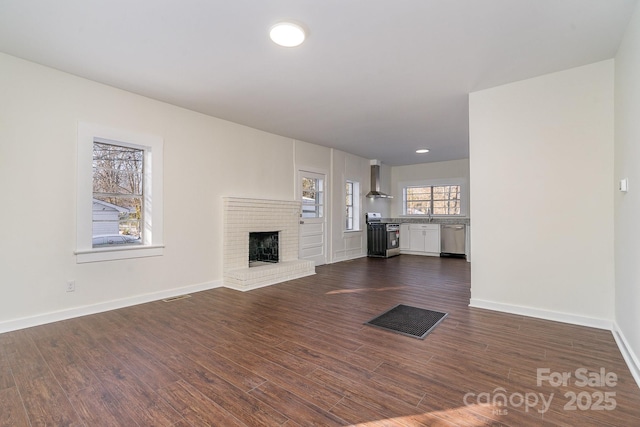 unfurnished living room with dark wood-style floors, a brick fireplace, visible vents, and baseboards