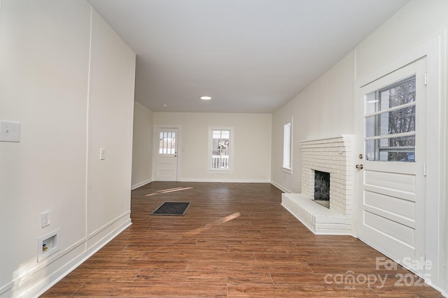 unfurnished living room with a brick fireplace and dark wood-type flooring