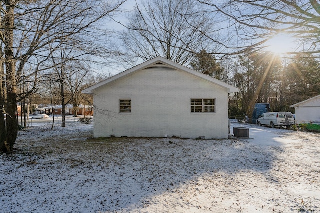 snow covered property with central AC and brick siding