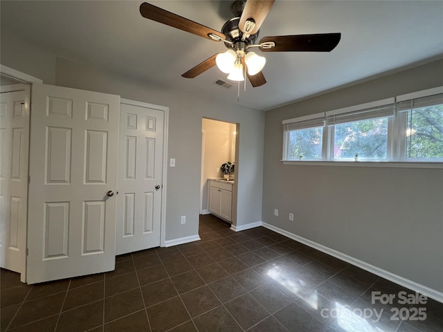 unfurnished bedroom featuring dark tile patterned floors, a closet, ceiling fan, and connected bathroom