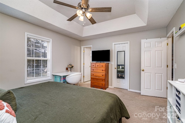 bedroom featuring light carpet, a textured ceiling, a raised ceiling, and ceiling fan