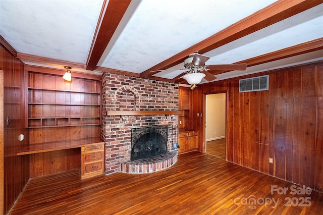 unfurnished living room featuring built in shelves, beam ceiling, wood walls, built in desk, and a fireplace