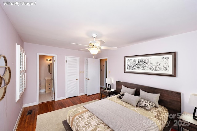 bedroom with two closets, dark hardwood / wood-style floors, ceiling fan, and ensuite bathroom