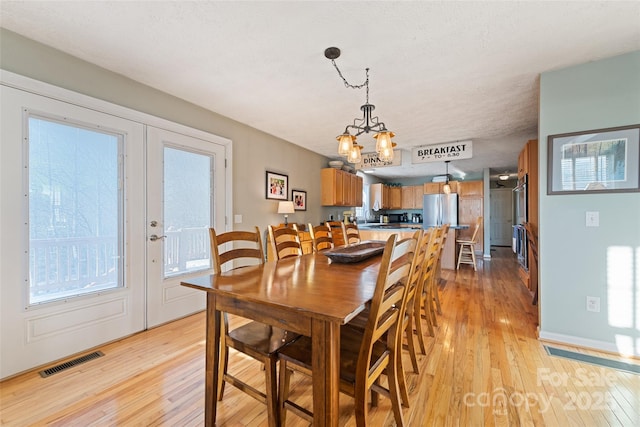 dining room featuring a textured ceiling, light hardwood / wood-style floors, a chandelier, and french doors