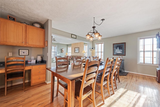 dining room featuring built in desk, ceiling fan with notable chandelier, light hardwood / wood-style flooring, and a textured ceiling